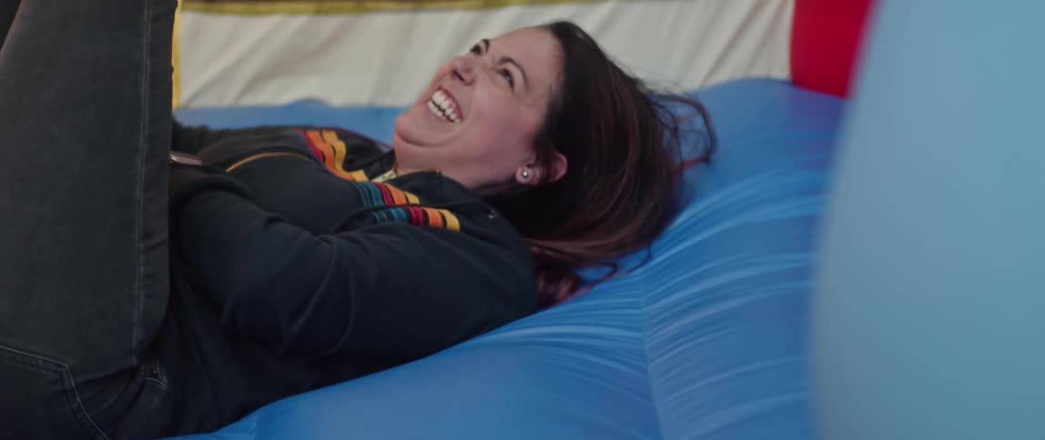 A woman lies on a mattress and laughs as she plays with her child