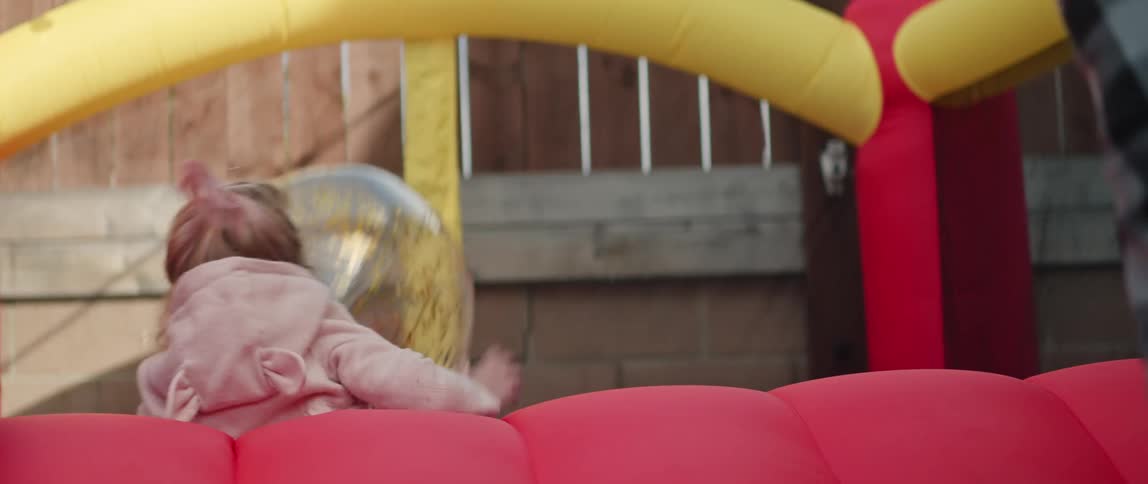 Parent throws clear inflated ball toward daughter and son on inflated bounce house