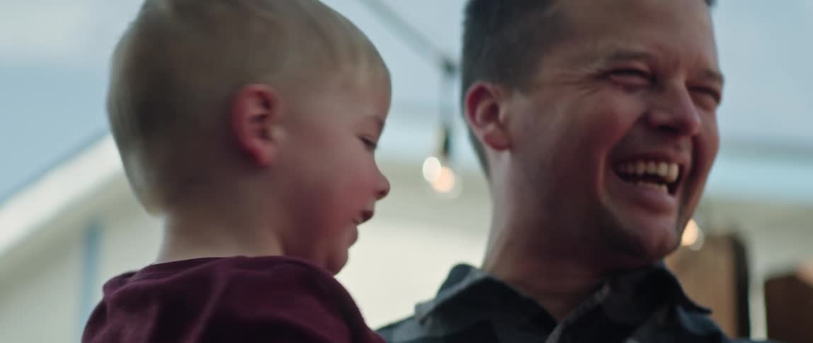 A man holding his son at home laughs with his son who is pointing