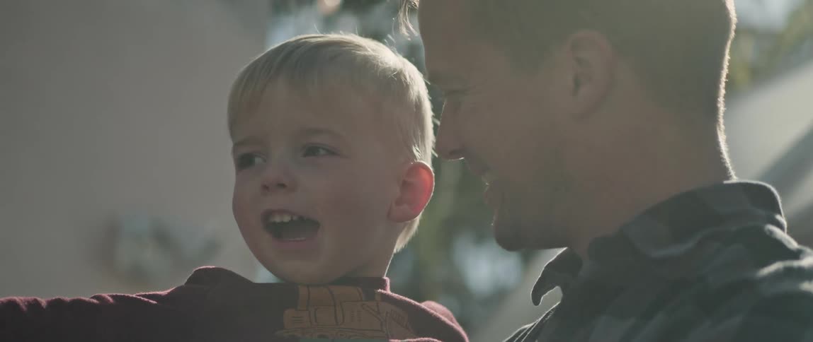 A father holding his son in his arms while the boy points at something ahead of them and they smile