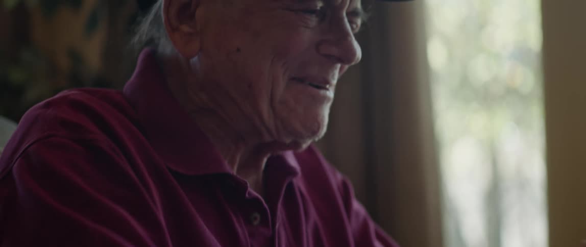 An elderly man smiles while writing notes before putting on his glasses