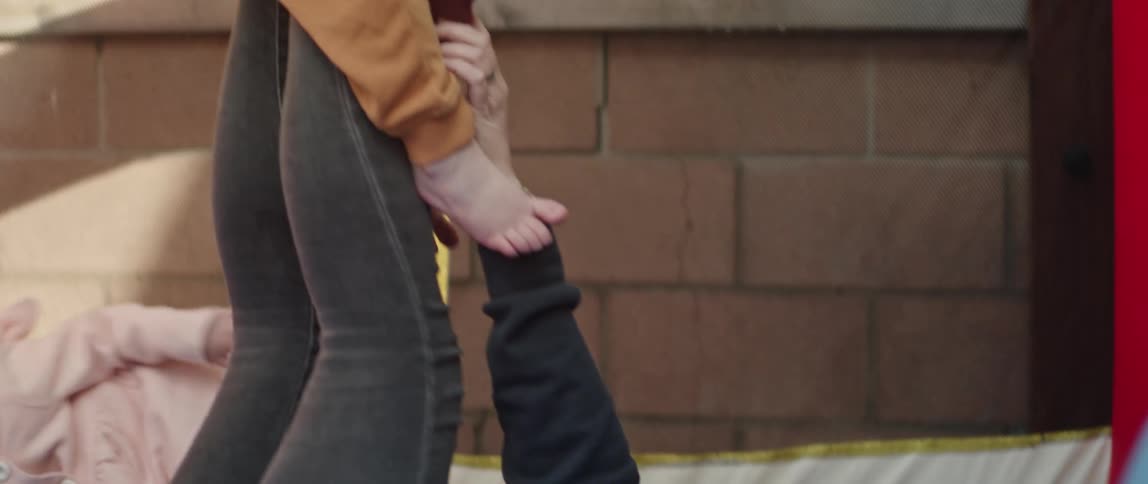 A mother plays with her son outdoors with him on her feet