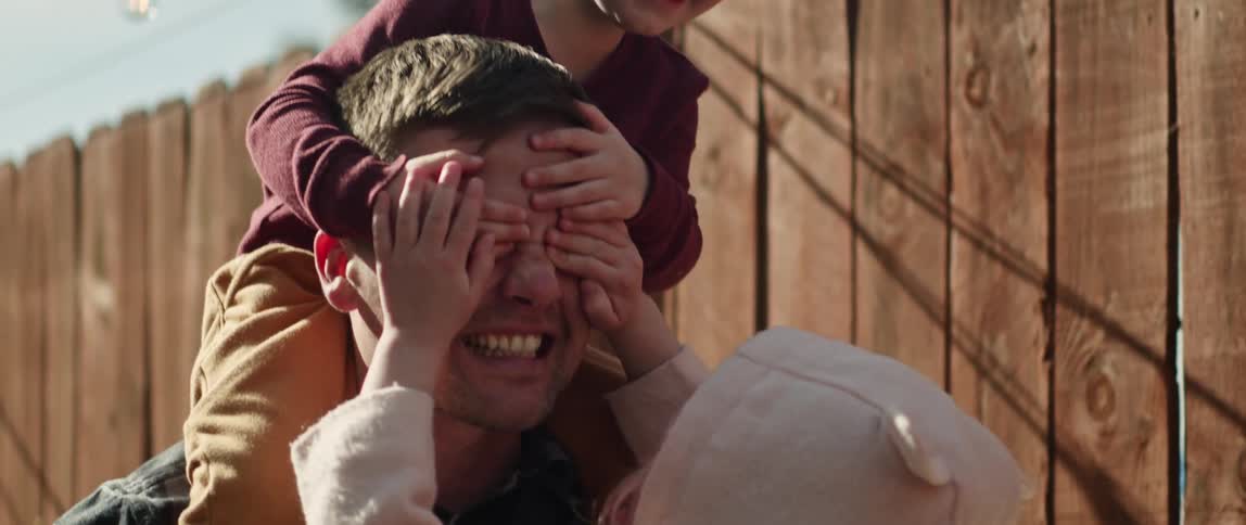 Father playing with toddler children son is sitting on dads shoulders and covering his eyes while dad is holding daughter in arms