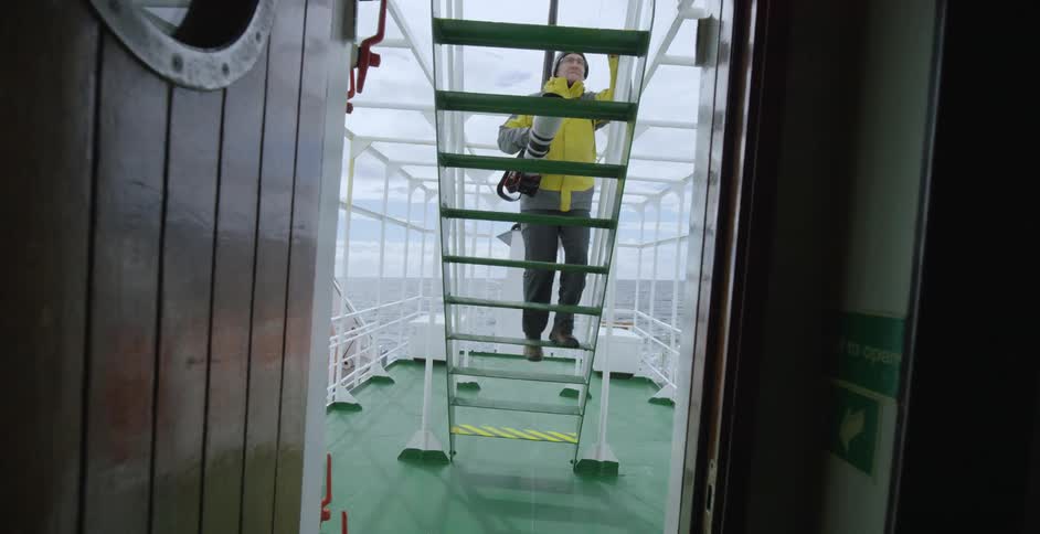 A man climbs steps on a ship with a camera