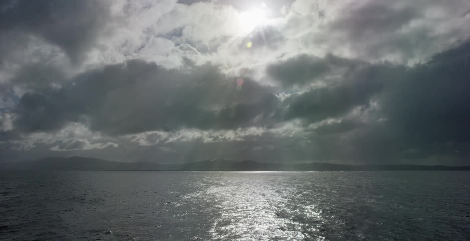 The sun casting rays through heavy clouds over the ocean