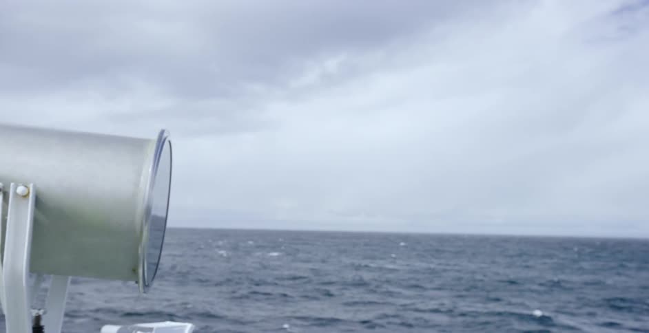 A man is standing near the spotlight of a ship sailing