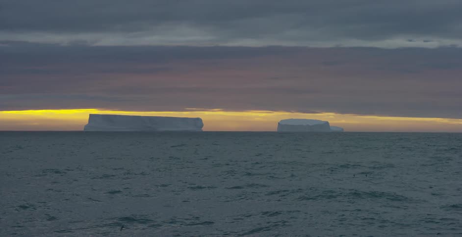 Icebergs floating in an ocean at sunset