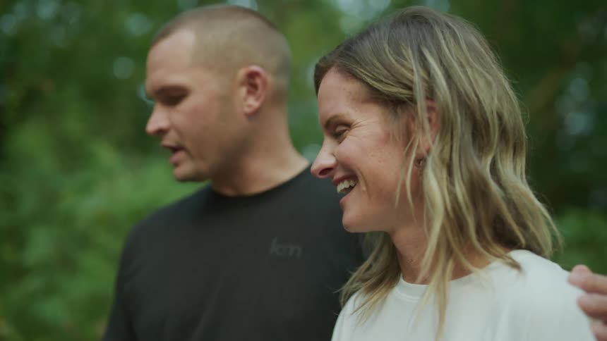 A man has his arm around a woman while they stand outside talking and looking at something