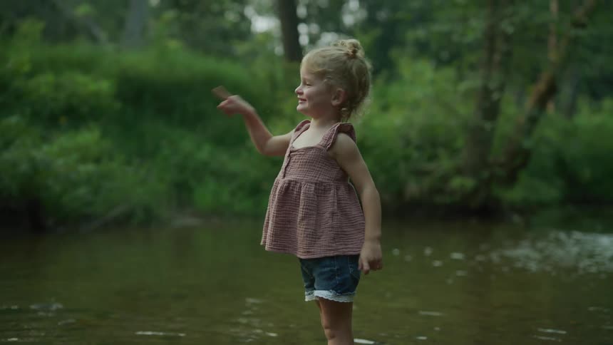 Female child standing in lake smiling and pointing into the water