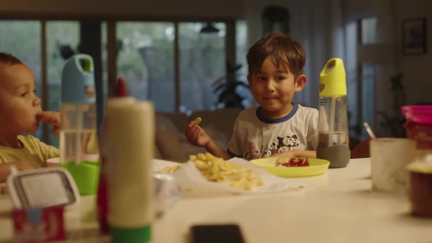 Two young boys sit at a dining table while consuming some food