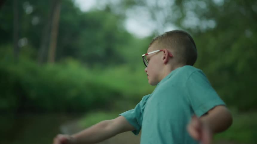 A boy wearing glasses throwing a skipping rock onto water