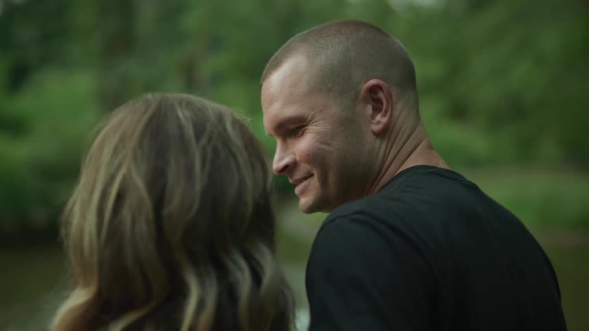 Young couple standing in front of a lake look at each other lovingly