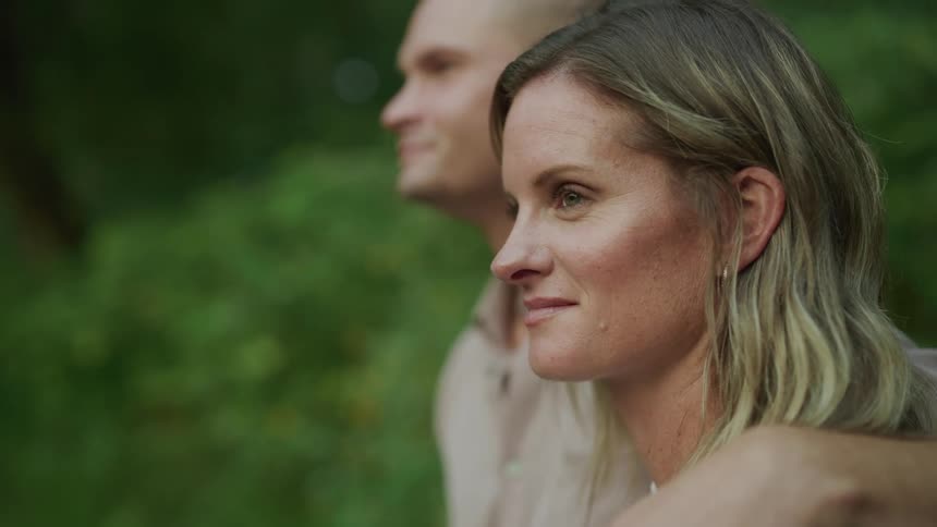 Young mom and dad standing near a lake looking out at it smiling relaxed