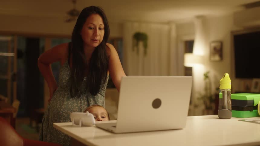Pregnant woman stands in the living room talking at someone on a video call through a laptop