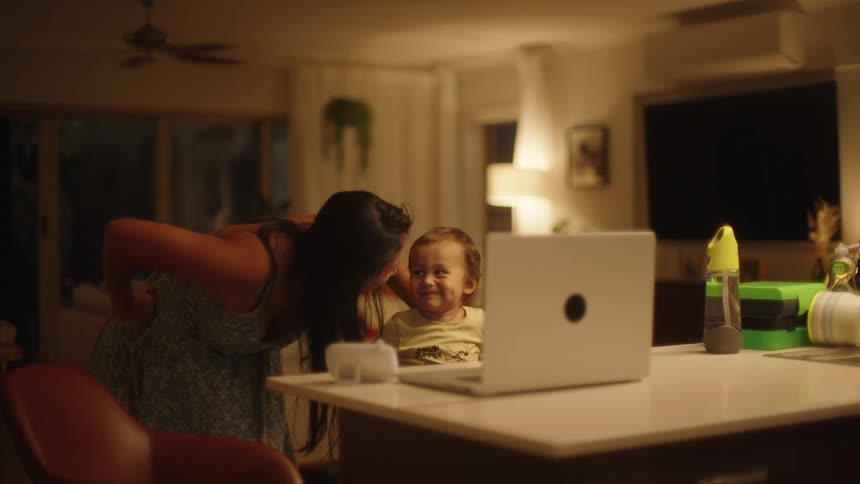 Happy family gathered on the living room smile and laugh at someone on a video call through a laptop