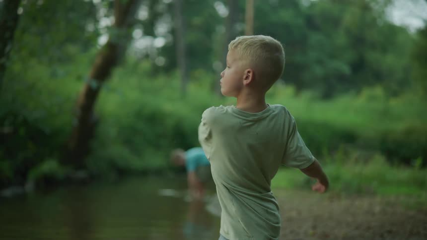 A young boy throws a rock in an attempt to skip it across a creek