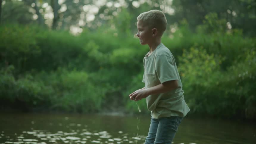 Young boy standing in lake with pant legs rolled up skipping rocks