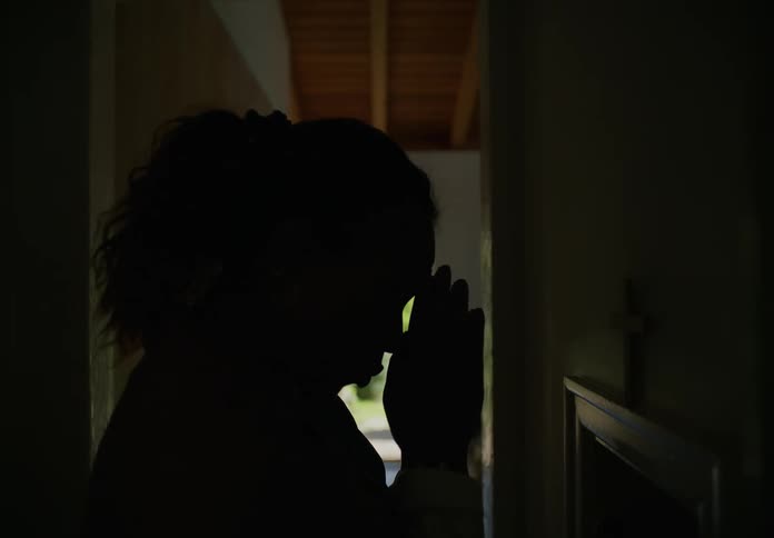 Silhouette of a young woman praying after entering her home