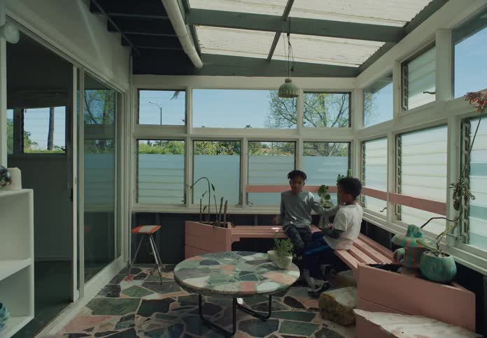 Two boys are sitting on an indoor patio bench as one boy pretends to hit the other with boxing moves
