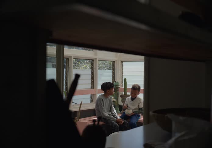 Two boys sitting on a counter one boy eating while the other sits there talking to him