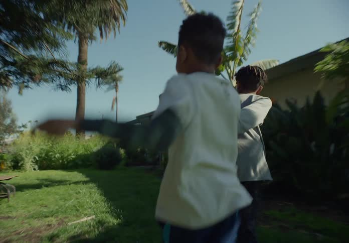 A boy running in the yard pulling his little brother behind him on a bright sunny day