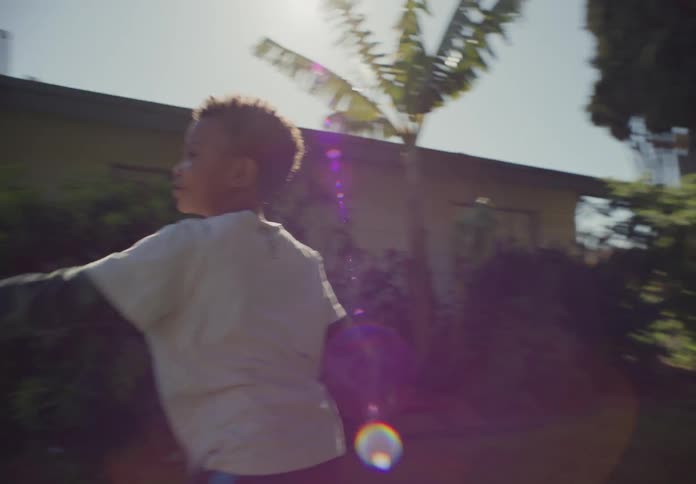 Two young boys chase each other and pretend to fight while outside in their yard