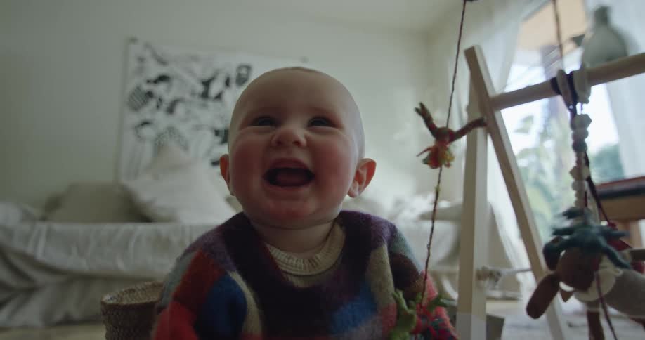 A baby girl sitting on the floor playing with a toy smiling and laughing