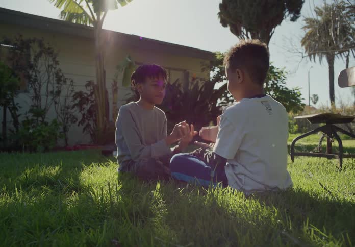 Two tween brothers on the front lawn sitting in the grass and playing