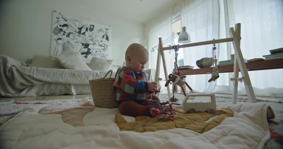 A baby sitting on the floor on a baby blanket while she plays with a toy in her hand