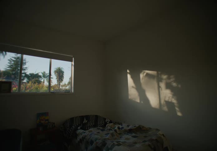 A bed in a bedroom covered in blankets with a three framed window with trees outside