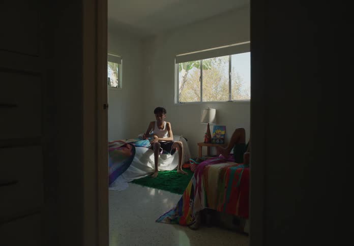 Two boys flop on beds indoors under a window