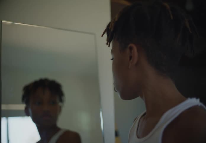 Teenage boy with dreadlocks and white undershirt looks in a mirror