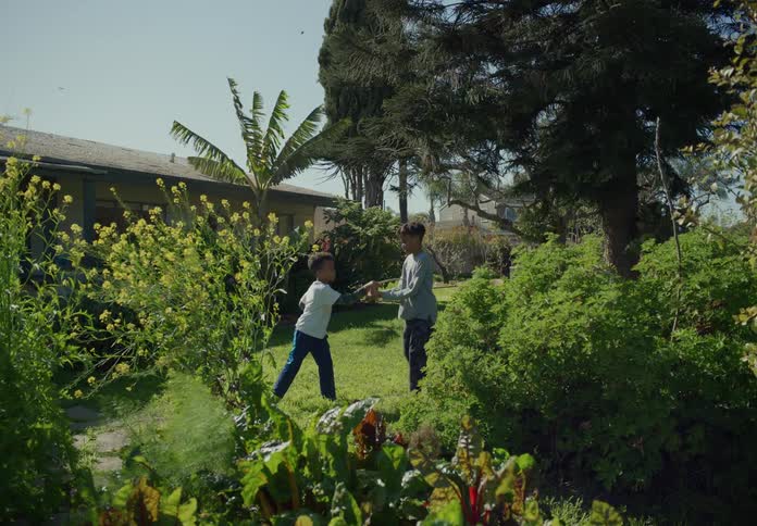 Big brother plays defense as little brother attacks with a stick sword in the yard on a windy day