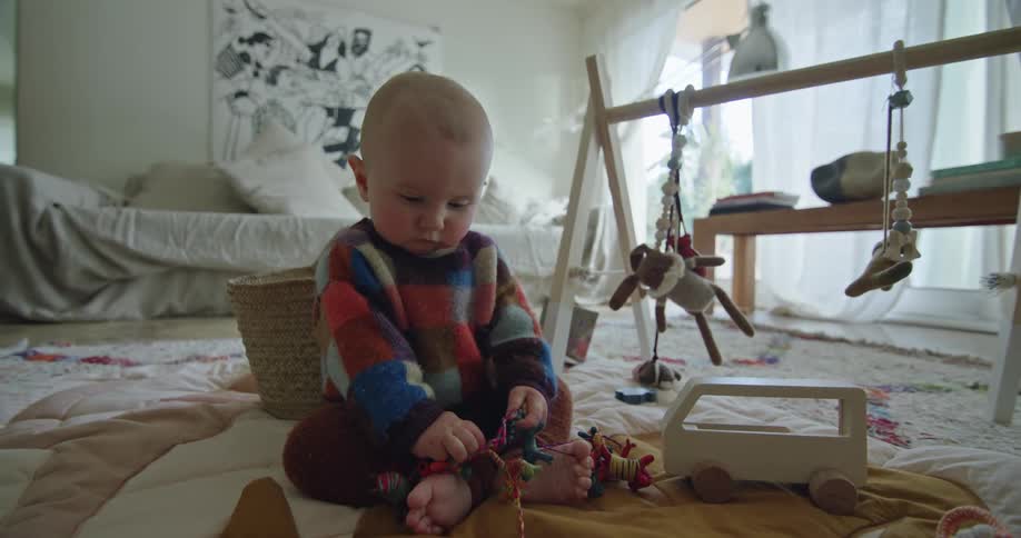 A baby girl sitting on the floor on a baby blanket playing with toys in front of her