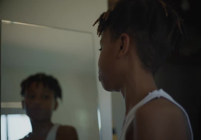 A boy standing in front of a mirror flexing his arm muscles then turning sideways and looking straight