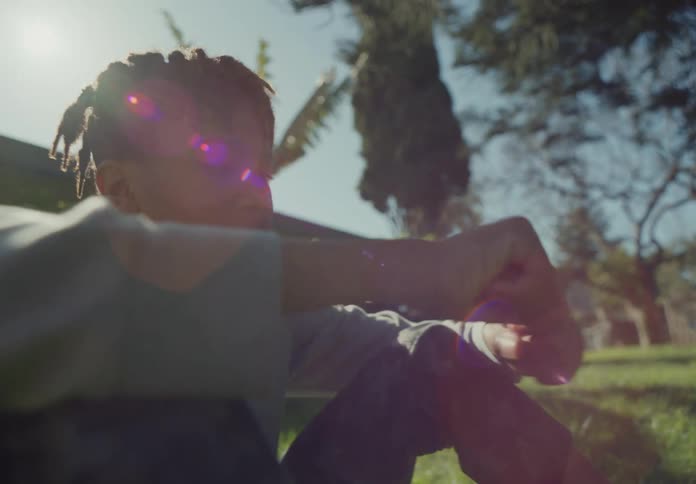 Youth sits on lawn playing with object near house on sunny day