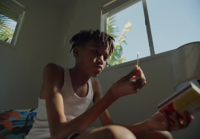 Bored young boy lights matches while sitting on a room at home next to a window