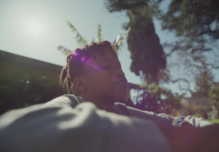A boy sits under a tree outside on a sunny day