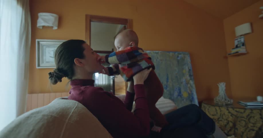 A woman holds a baby while sitting on a couch indoors