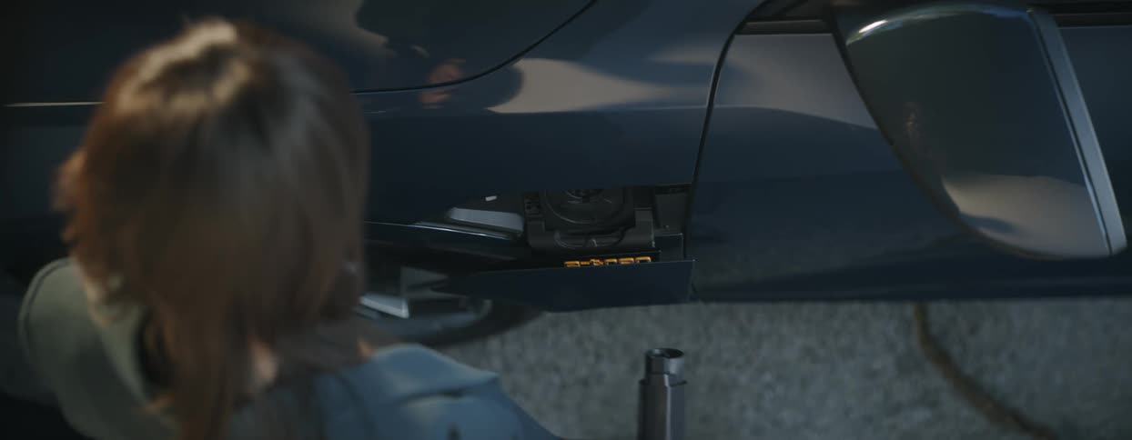 A woman steps up to her car and pulls out the electrical charging cable