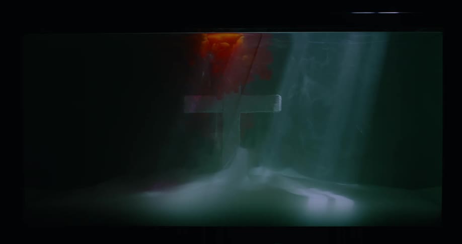 A white cross with red smoke above it as lights cast shadows acros it