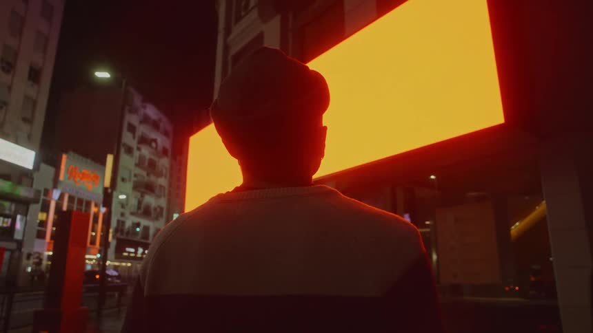 A man is standing in a downtown city during the night