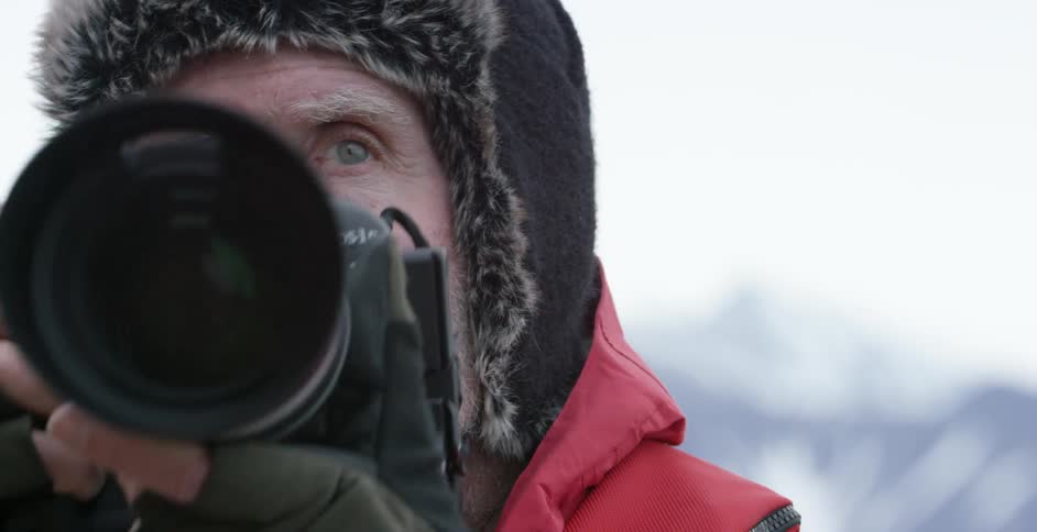 A bearded man lifts a camera