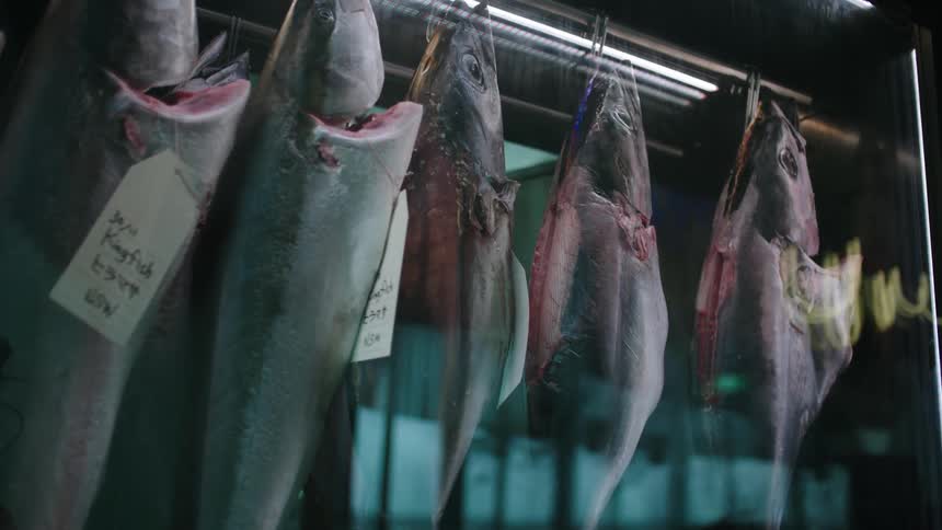 Rows of gutted fish hanging on the storefront window of a street shop