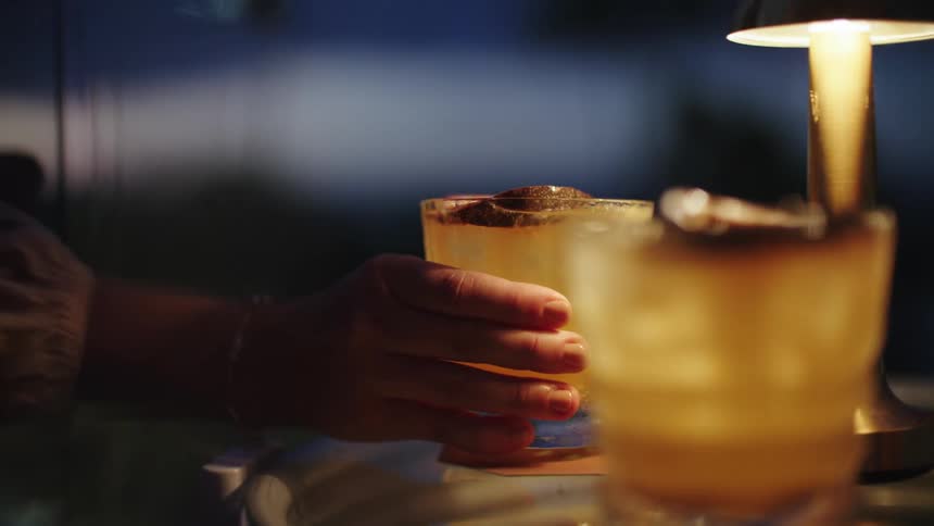Two full glasses next to a small lamp as a person grabs the glass to drink from