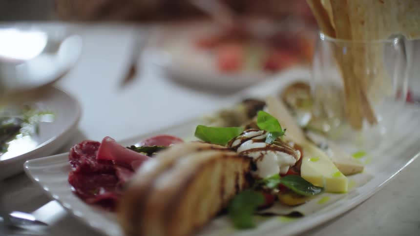 Artfully plated food sits on dining table covered with a white tablecloth as person eats