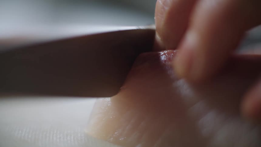 A person holds a piece of uncooked meat while slicing it with a knife