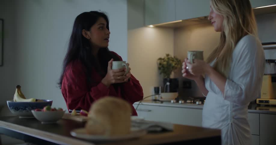 Two female having a conversation drinking coffee in a kitchen