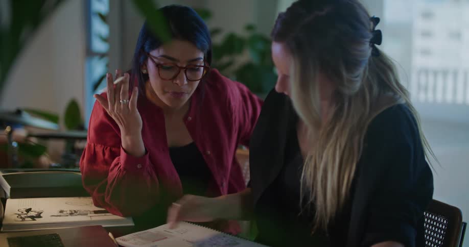 Two coworkers sit at table discussing designs