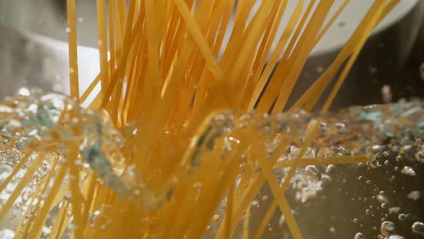 Fettuccine noodles are falling into a pot with boiling water